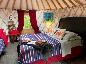 A tented accommodation room with a bed, a chair, a table, and a painting on the wall.