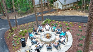 A circular outdoor seating area with stone flooring, surrounded by trees and a small building with a metal roof.