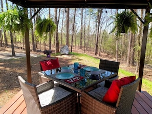 An outdoor dining area with wicker furniture, glass tables, and red cushions.