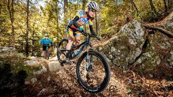 A mountain biker navigating a rocky trail in a forested area.