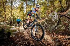 Un ciclista de montaña recorre un sendero pedregoso en una zona boscosa.
