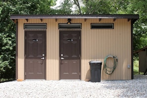 A small building with two doors, a trash can, and a hose.
