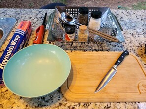 Una encimera de cocina con una tabla de cortar, un cuchillo, un bol, una caja de Reynolds Wrap, un rallador y algunas especias.