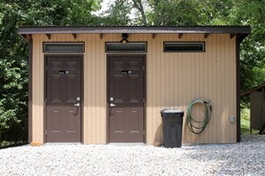 Un petit bâtiment avec deux portes, une poubelle et un tuyau d’arrosage.