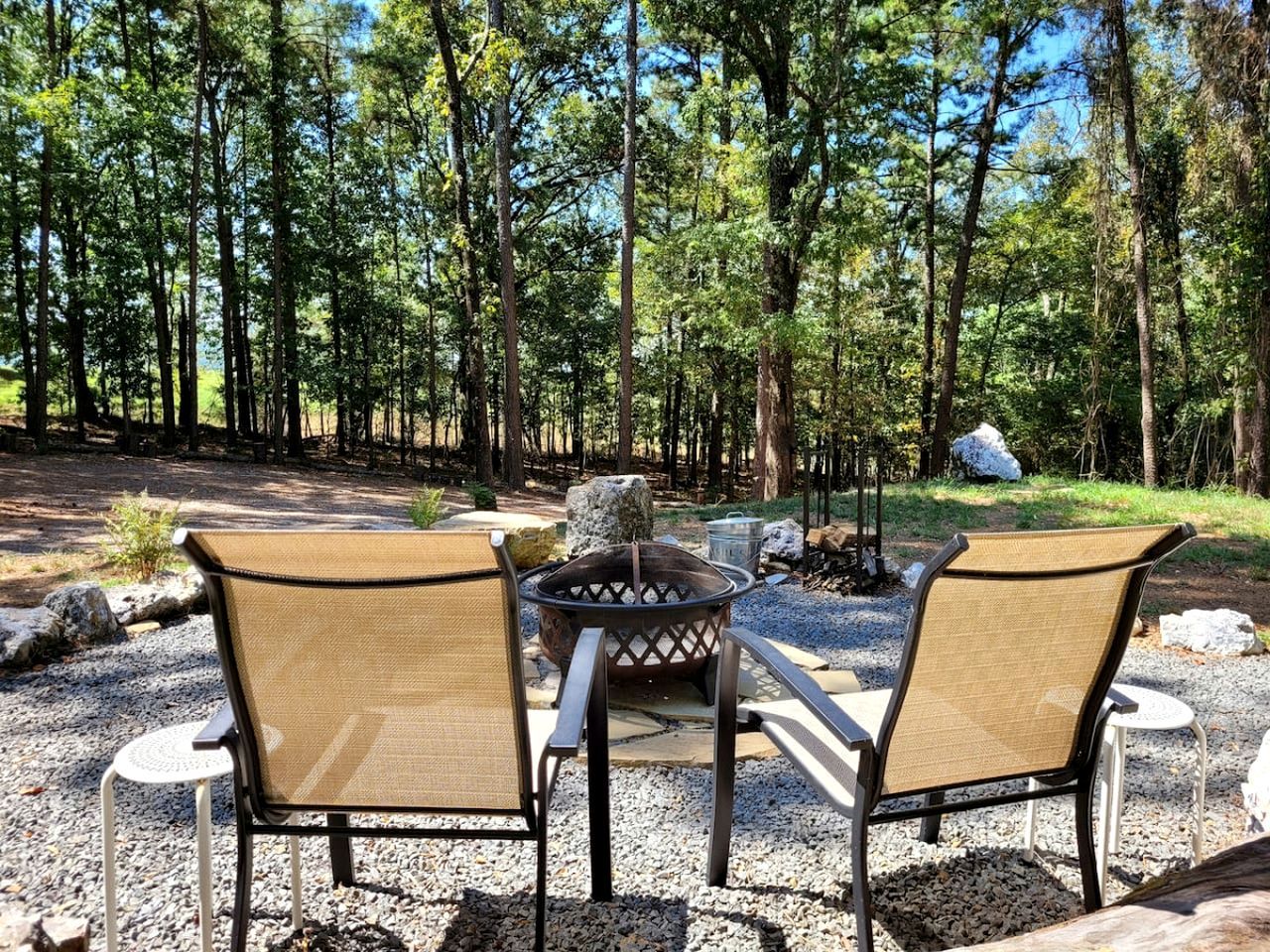 Une terrasse avec deux chaises et un foyer, située dans une zone boisée.