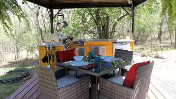 An outdoor kitchen with a grill, sink, and dining area with wicker chairs and a table set for two.
