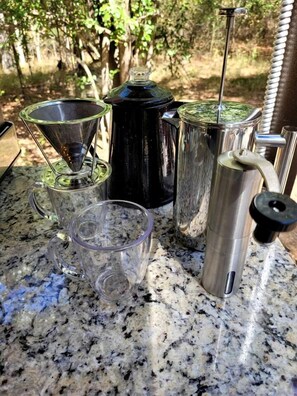 Una encimera de cocina con una cafetera, una jarra de vidrio, una taza de vidrio y un hervidor metálico.