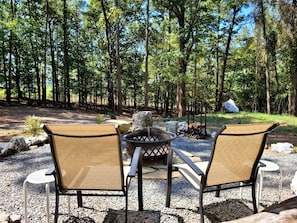 A patio with two chairs and a fire pit in a forested area.