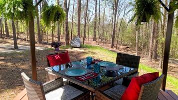 An outdoor dining area with wicker furniture, glass tables, and red cushions.