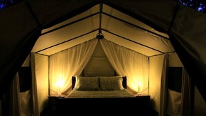 Ein Zeltraum mit einem Bett, zwei Nachttischlampen und transparenten Vorhängen.