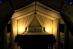 Une pièce aménagée comme une tente, avec un lit, deux lampes de chevet et des rideaux légers.