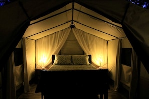 Ein Zeltraum mit einem Bett, zwei Nachttischlampen und transparenten Vorhängen.