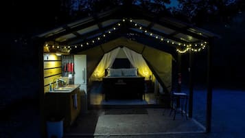 A tented accommodation with a kitchenette, a bed, and string lights.