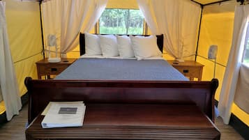 A tented room with a bed, bedside tables, a fan, and a window.