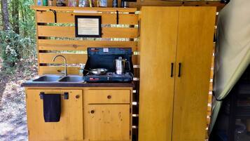 A compact outdoor kitchen with a sink, stove, and storage cabinets.