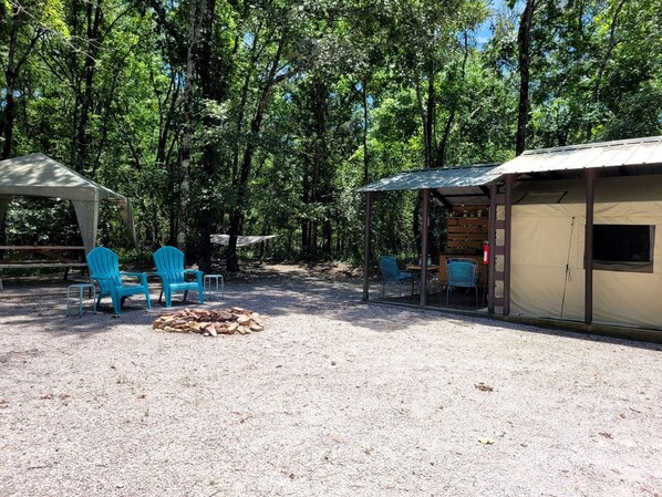 Un terrain de camping doté d’un espace de repos couvert, d’un foyer et d’un petit bâtiment.