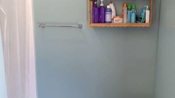 A bathroom with a shower, a wooden shelf with toiletries, and a small wooden table.