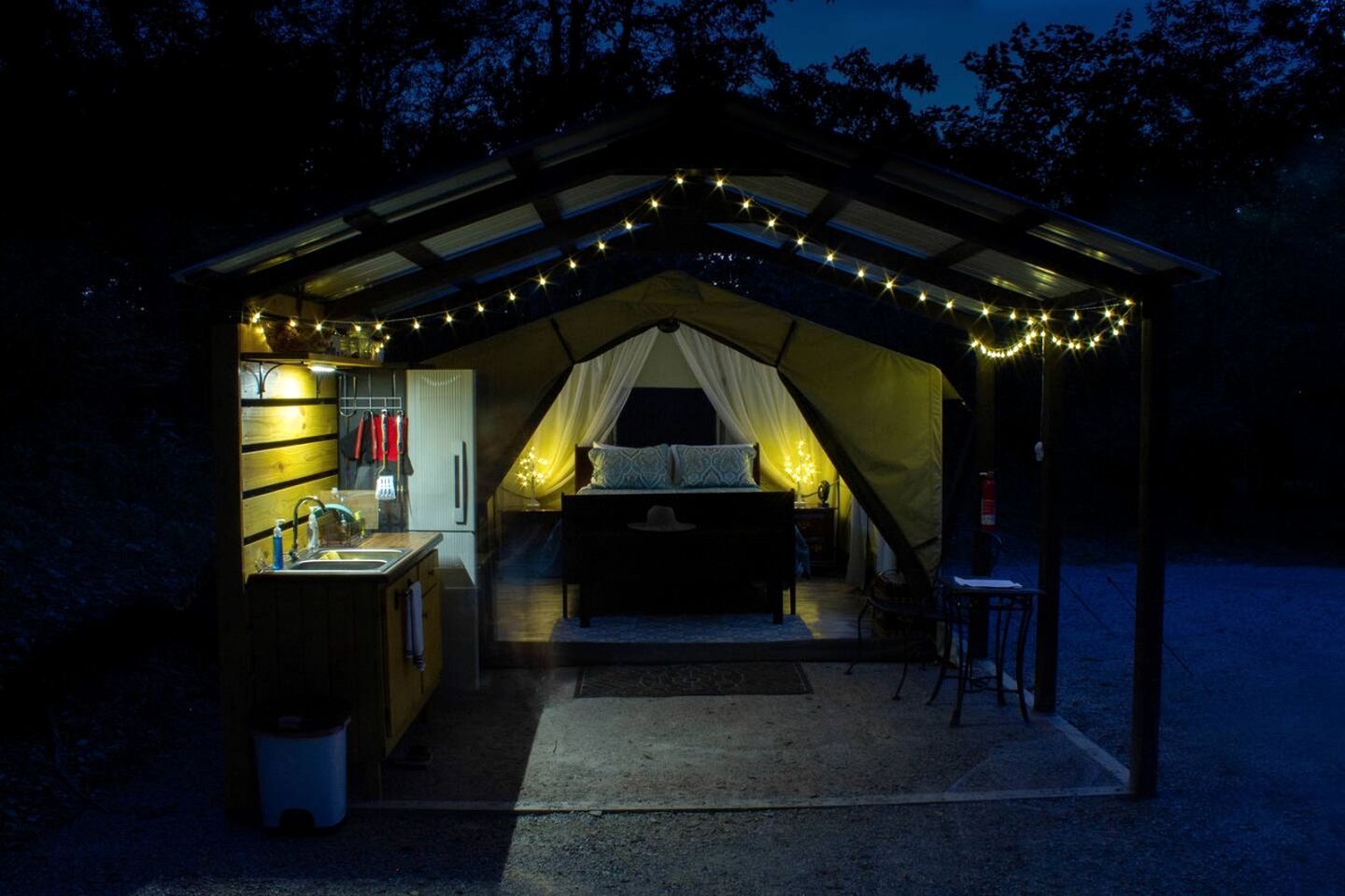 Alojamiento en carpa con kitchenette, una cama y luces colgantes.