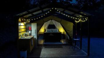 Alojamiento en carpa con kitchenette, una cama y luces colgantes.