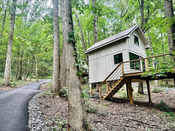 A wooden cabin with a staircase, surrounded by trees and a path.