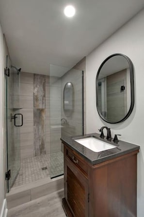 Un baño moderno con cabina de ducha de vidrio, tocador de madera y un espejo grande.