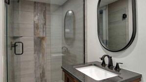 Un baño moderno con cabina de ducha de vidrio, tocador de madera y un espejo grande.