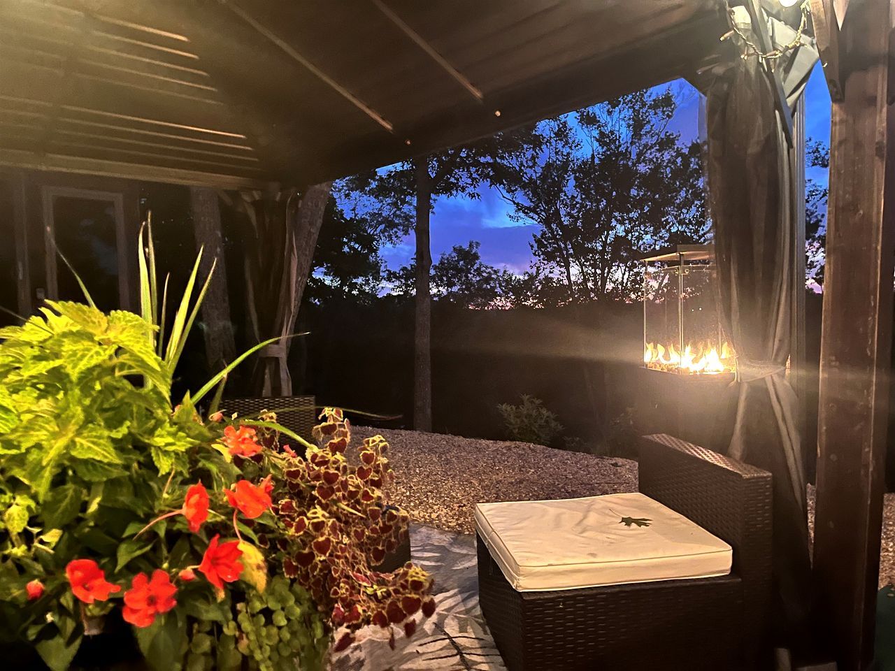 Un área de estar al aire libre con mesa y sillas, rodeada de plantas y un hogar para fuego.