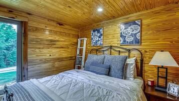 Ein Schlafzimmer einer Holzhütte mit Bett, Kissen, einer Leitern, einem Nachttisch mit Lampe und einer Uhr.