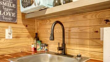 A wooden interior with a stainless steel sink, a faucet, and a shelf above containing a sign and various items.