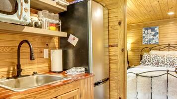 Una cabaña de madera acogedora con kitchenette, que incluye un lavamanos, un microondas y un refrigerador.