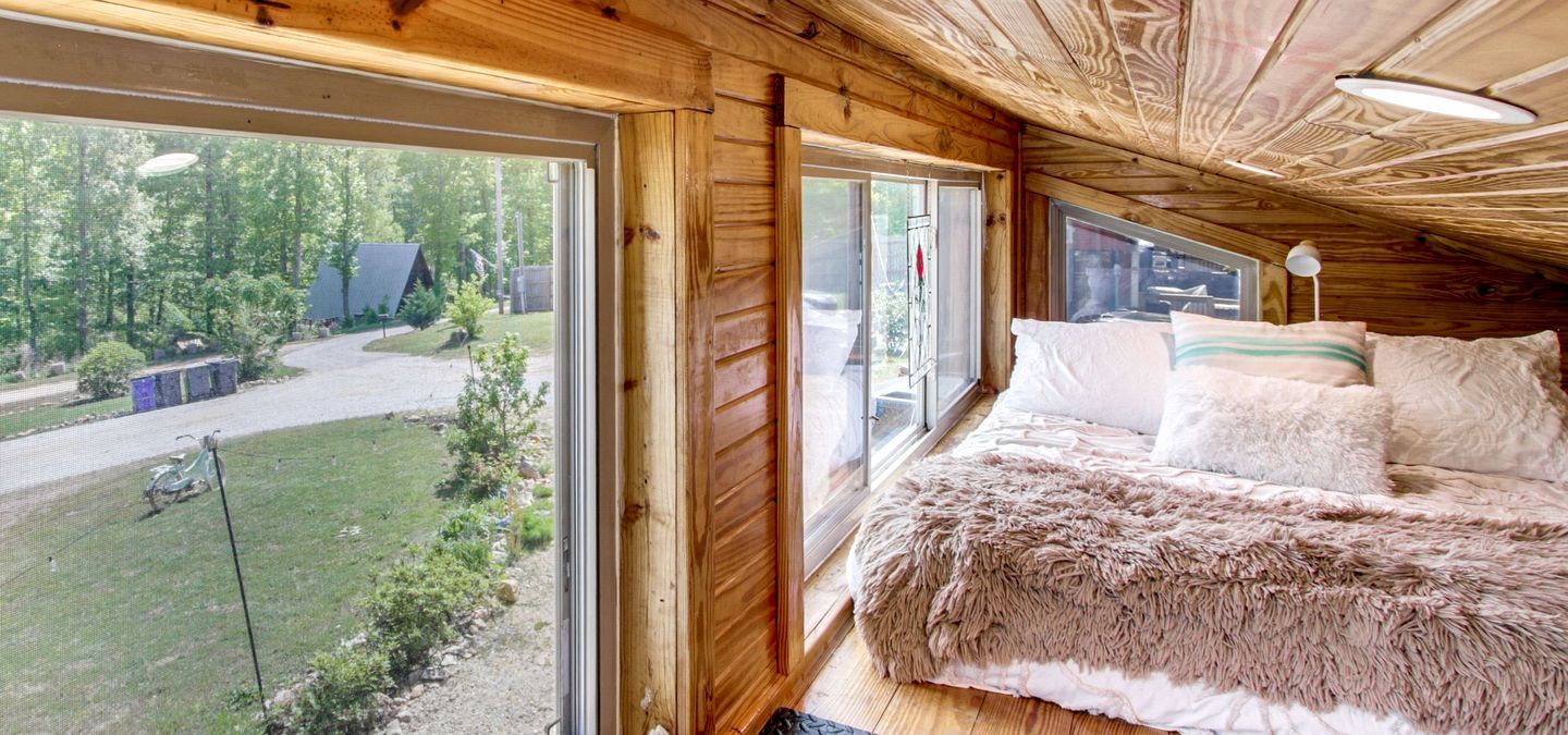 Une chambre dans une cabane en bois, avec un lit, une fenêtre et une vue sur une zone boisée.