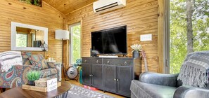 A cozy cabin interior with a television, wooden walls, a sofa, a cabinet, and a mirror.