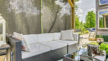 A wicker sofa with cushions, a glass table with a wine glass, and a lantern.