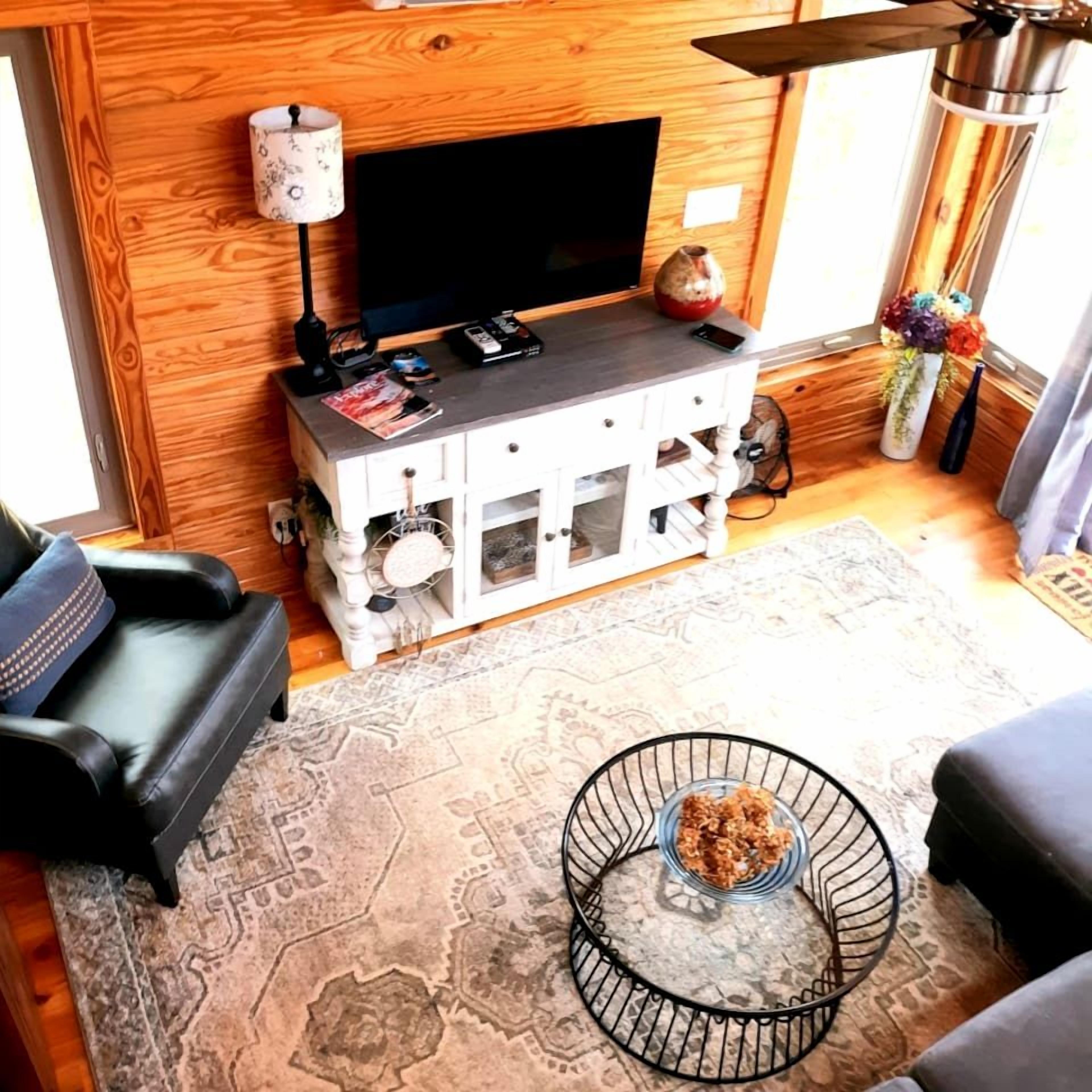 A living room with a TV, wooden wall paneling, a sofa, a coffee table, and a decorative vase.