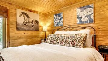 A wooden-paneled room with a bed, a painting of a horse, and two floral paintings on the wall.