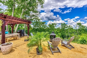 An outdoor patio with a pergola, wooden chairs, a table, and a grill.