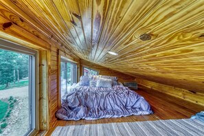 Ein Schlafzimmer mit einem Bett, Holzwänden und Blick durch ein großes Fenster.