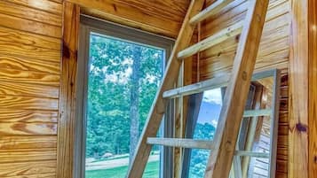Interior de madera con una escalera que lleva a una ventana, un banco y una puerta.
