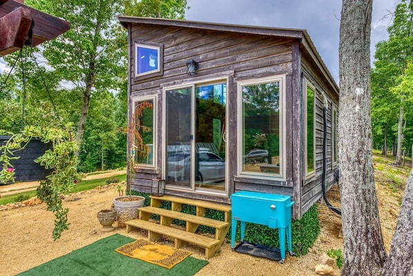 A rustic wooden cabin with large windows, a small porch, and a blue cooler.