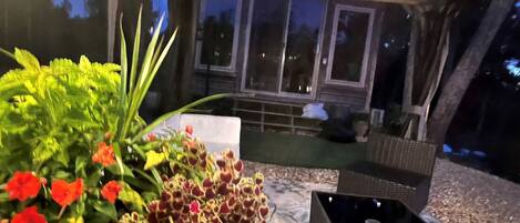 An outdoor seating area with a table and chairs, surrounded by potted plants and a view of the night sky.