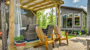 A wooden deck with two Adirondack chairs, a grill, and a small cabin with large windows.