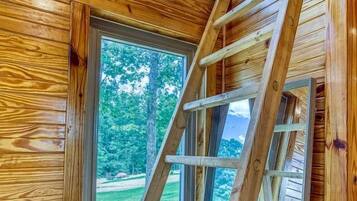 A wooden interior with a ladder leading to a window, a bench, and a door.