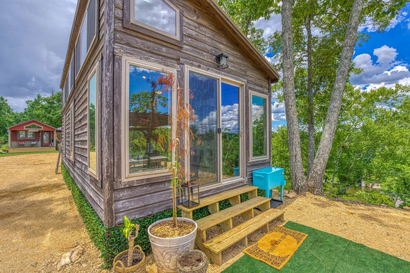 Una cabaña rústica de madera con ventanas amplias, un porche pequeño y una zona de estar exterior azul.