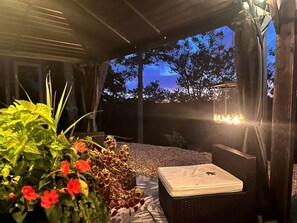 Un espace extérieur aménagé avec une table et des chaises, entouré de plantes et agrémenté d’un foyer.