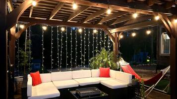 An outdoor seating area with a wooden pergola, string lights, and a hammock.