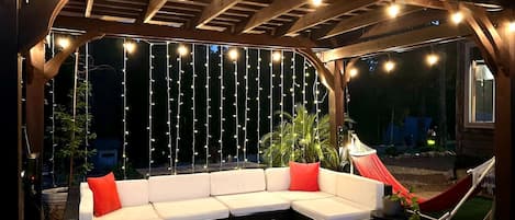 Un espace extérieur aménagé avec une pergola en bois, des guirlandes lumineuses et un hamac.