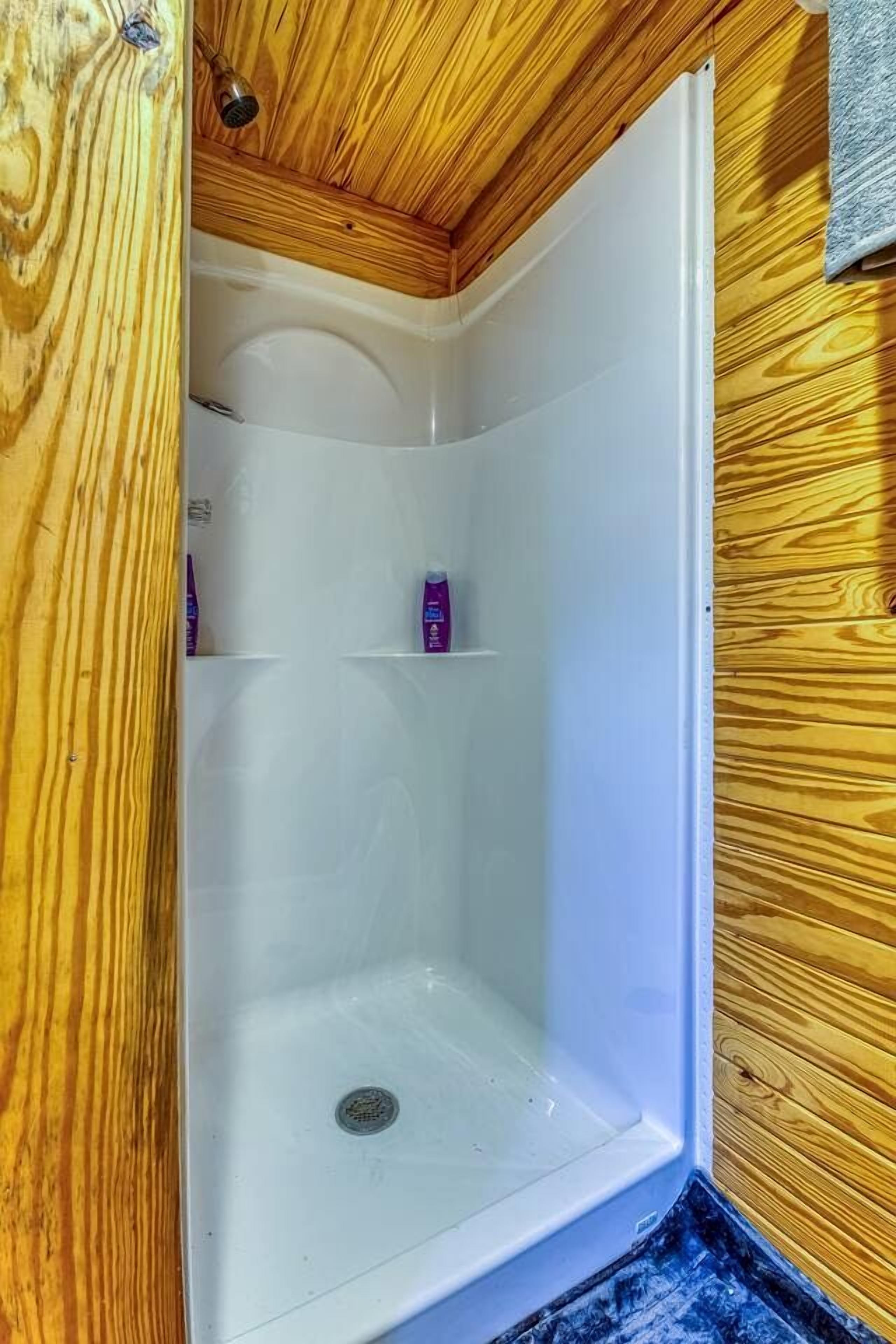 Ducha con techo y paredes de madera, una bañera blanca y un estante con artículos de aseo.