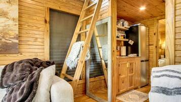 L’intérieur chaleureux d’un chalet, avec un revêtement mural en bois, une échelle, un réfrigérateur et un canapé.