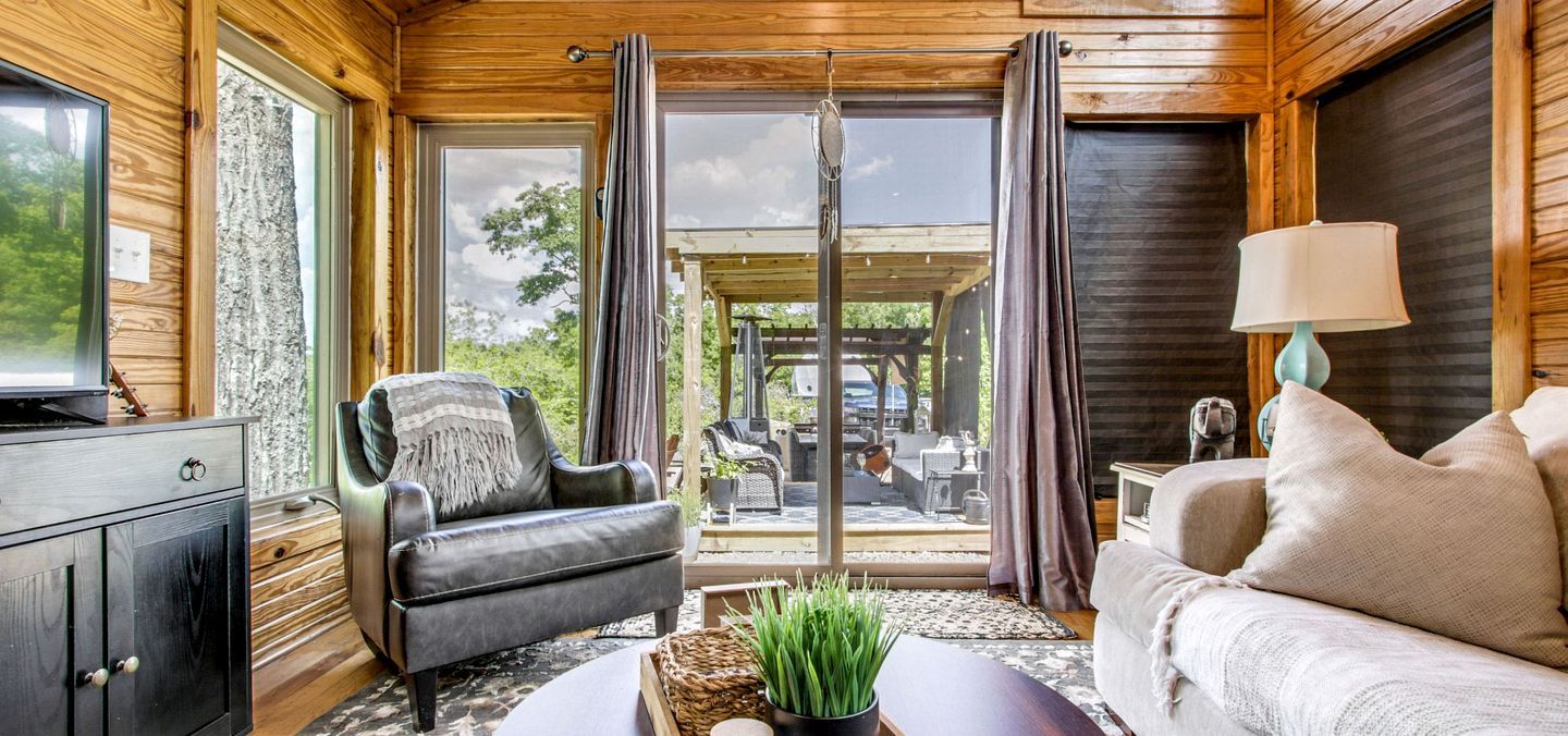 Un cuarto acogedor con un sillón de cuero, un sofá, un televisor y vistas al exterior a través de amplios ventanales.