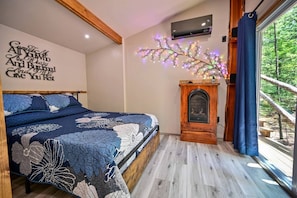 Una camera da letto con un letto, un condizionatore fissato al muro, un elemento decorativo a parete, un caminetto e una finestra vista alberi.